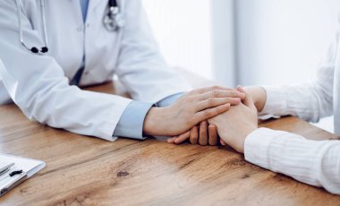 Doktor ve hasta klinikteki ahşap masada oturuyorlar. Kadın doktorların elleri güven veren kadınlarındır. Tıp konsepti.