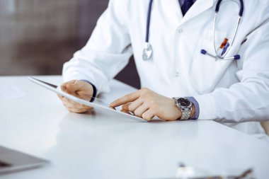 Bilinmeyen erkek doktor klinikteki tablet bilgisayarla yakın planda çalışıyor. İşteki genç doktor. Mükemmel sağlık hizmeti, tıp konsepti.