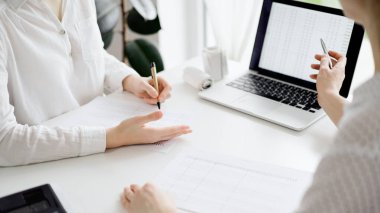 Beyaz masadaki vergileri saymak için dizüstü bilgisayar kullanan iki muhasebeci. İş kadını elinde kalemle ekranı işaret ediyor. İş denetimi ve finans alanında takım çalışması.