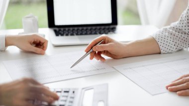 Ofisteki bir müşteriyle ya da meslektaşıyla vergi saymak için hesap makinesi ve dizüstü bilgisayar kullanan bir muhasebeci. İş denetimi ve finans alanında takım çalışması.