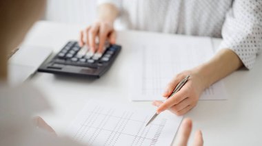 Ofisteki bir müşteriyle ya da meslektaşıyla vergi saymak için hesap makinesi ve dizüstü bilgisayar kullanan bir muhasebeci. İş denetimi ve finans alanında takım çalışması.