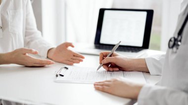Doktor ve hasta klinikteki beyaz masada oturup bir şeyler tartışıyorlar. Kadın hekim bir kayıt formunu doldururken dinliyor. Tıp konsepti.