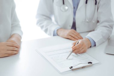 Doktor ve hasta birbirlerine yakın otururken sağlık sorularını tartışıyorlar ve klinikteki masada pano kullanıyorlar, sadece ellerini kapatıyorlar. Tıp konsepti.