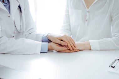 Doktor ve hasta klinikteki masada yan yana oturuyorlar. Kadın doktorlara odaklan. Kadına güven veren eller, sadece eller, yakın çekim. Tıp konsepti.