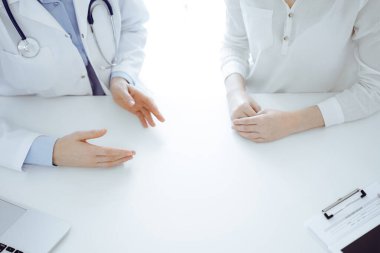 Doktor ve hasta klinikteki masada yan yana otururken sağlık sorunlarını tartışıyorlar. Sadece ellerinizi yakın tutun. Tıp konsepti.