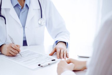 Doktor ve hasta klinikteki masada karşılıklı oturuyorlar. Kadın doktorların ellerinin tıbbi geçmiş kayıtlarını doldurması ya da kontrol listesi üzerinde yoğunlaşacağız. Kapat. Tıp konsepti.