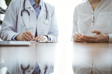 Doktor ve hasta klinikteki ahşap masada yan yana oturuyorlar. Kadın doktorlar kayıt formunu dolduruyorlar. Tıp konsepti.