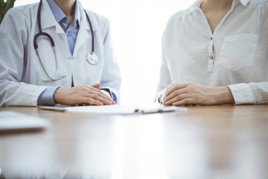 Doktor ve hasta, klinikteki ahşap masada yan yana otururken bir şey tartışıyorlar. Tıp konsepti.