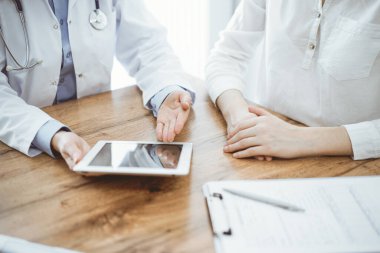 Doktor ve hasta klinikteki ahşap masada oturuyorlar. Dizüstü bilgisayar monitörüne bakan kadın doktorlar, kapatın. Tıp konsepti.