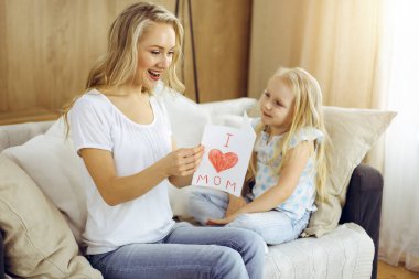 Güneşli dairede anneler günün kutlu olsun. Çocuk kızı annesini tebrik ediyor ve ona kalp çizimiyle kartpostal atıyor. Aile kavramı.