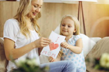 Güneşli dairede anneler günün kutlu olsun. Çocuk kızı annesini tebrik ediyor ve ona kalp çizimiyle kartpostal atıyor. Aile kavramı.