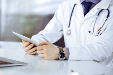 Bilinmeyen erkek doktor klinikteki tablet bilgisayarla yakın planda çalışıyor. İşteki genç doktor. Mükemmel sağlık hizmeti, tıp konsepti.