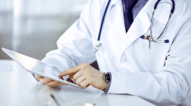 Bilinmeyen erkek doktor klinikteki tablet bilgisayarla yakın planda çalışıyor. İşteki genç doktor. Mükemmel sağlık hizmeti, tıp konsepti.
