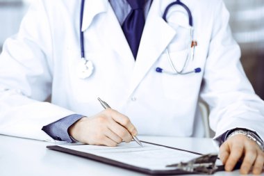 Bilinmeyen erkek doktor, klinikte, yakın planda pano ile oturuyor ve çalışıyor. İşteki genç doktor. Mükemmel sağlık hizmeti, tıp konsepti.