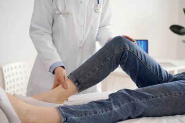 Doktor ve hasta klinikte olağan sağlık kontrolündeler. Terapist genç bir kadının dizini muayene ediyor. Tıp konsepti .