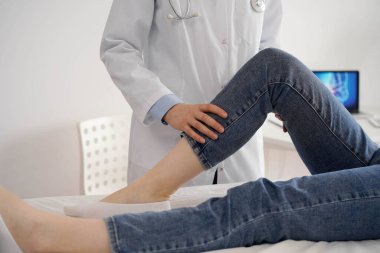 Doktor ve hasta klinikte olağan sağlık kontrolündeler. Terapist genç bir kadının dizini muayene ediyor. Tıp konsepti .