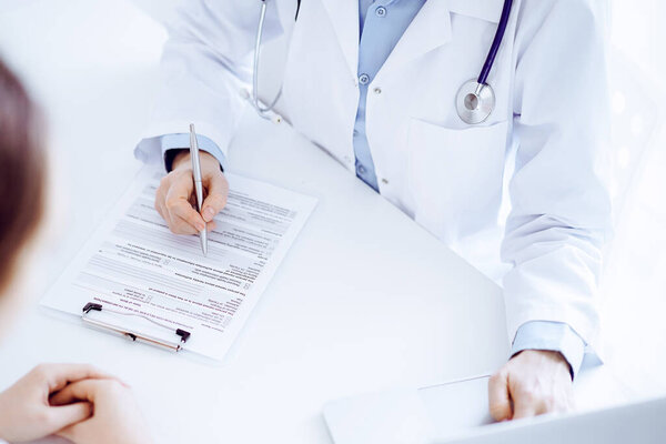 Doctor and patient discussing something and using laptop while sitting opposite each other at the desk in clinic office. Perfect medical service and medicine concept.
