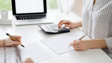 Hesap makinesi ve dizüstü bilgisayar kullanan iki muhasebeci vergileri ve gelir dengesini hesaplamak için beklerken makbuzlar da hesaplanmayı bekliyor. İş denetimi ve vergi kavramları.