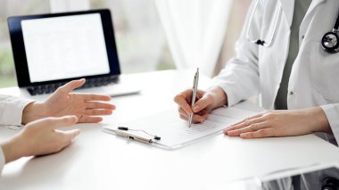 Doktor ve hasta klinikteki beyaz masada oturup bir şeyler tartışıyorlar. Kadın hekim bir kayıt formunu doldururken dinliyor. Tıp konsepti.