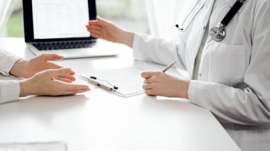 Doktor ve hasta klinikteki beyaz masada oturup bir şeyler tartışıyorlar. Kadın doktor dizüstü bilgisayarın ekranına işaret ediyor. Tıp konsepti.