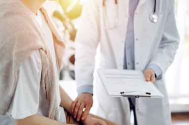 Doktor ve hasta klinikte. Bir yandan dostane bir doktor genç bir kadını muayene ederken diğer yandan tıbbi kayıtlarla dolu bir pano tutuyor. Tıp konsepti.