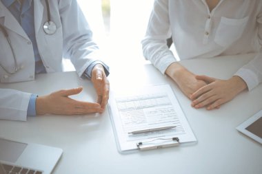 Doktor ve hasta birbirlerine yakın otururken sağlık sorularını tartışıyorlar ve klinikteki masada pano kullanıyorlar, sadece ellerini kapatıyorlar. Tıp konsepti.