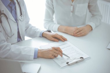 Doktor ve hasta birbirlerine yakın otururken sağlık sorularını tartışıyorlar ve klinikteki masada pano kullanıyorlar, sadece ellerini kapatıyorlar. Tıp konsepti.