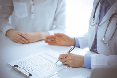 Doktor ve hasta birbirlerine yakın otururken sağlık sorularını tartışıyorlar ve klinikteki masada pano kullanıyorlar, sadece ellerini kapatıyorlar. Tıp konsepti.