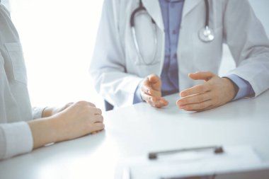 Doktor ve hasta klinikteki masada yan yana otururken sağlık sorunlarını tartışıyorlar. Sadece ellerinizi yakın tutun. Tıp konsepti.