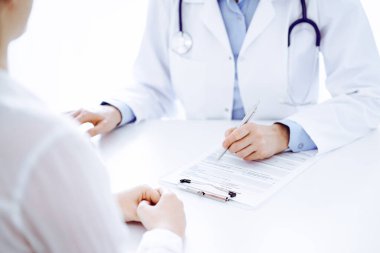 Doktor ve hasta bir şey tartışıyor ve klinikteki masada karşılıklı otururken dizüstü bilgisayar kullanıyorlar. Mükemmel tıbbi hizmet ve tıp konsepti.