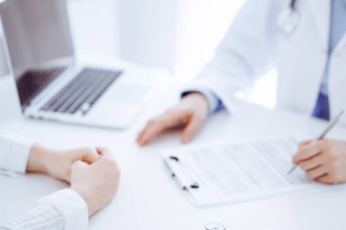 Arka planda karşılıklı oturan bir doktor ve hastanın önündeki tablet bilgisayarın üzerinde steteskop var. Tıp, sağlık hizmeti kavramı.