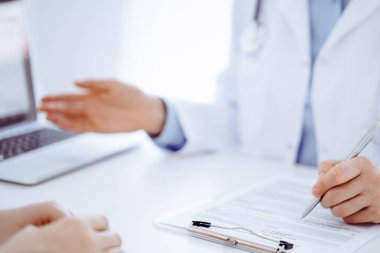 Doktor ve hasta klinikteki masada karşılıklı oturuyorlar. Kadın doktorların ellerinin tıbbi geçmiş kayıtlarını doldurması ya da kontrol listesi üzerinde yoğunlaşacağız. Kapat. Tıp konsepti.