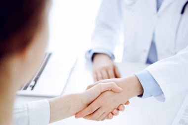 Klinikteki masada karşılıklı otururken doktor ve hasta el sıkışıyor. Sadece eller kapalı. Tıp konsepti.