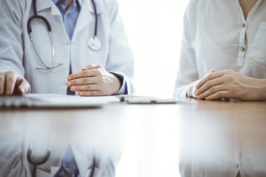 Doktor ve hasta laptoplarını kullanırken ve klinikteki ahşap masada yan yana otururken bir şeyler tartışıyorlar. Tıp konsepti.