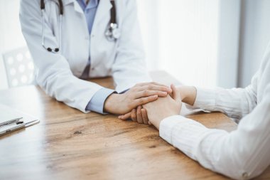 Doktor ve hasta klinikteki ahşap masada oturuyorlar. Kadın doktorların elleri güven veren kadınlarındır. Tıp konsepti.