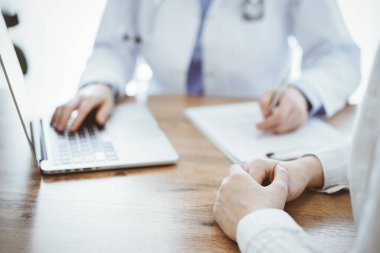 Doktor ve hasta oturmuş, dizüstü bilgisayar kullanırken ahşap masada bir şeyler tartışıyorlar. Hastaların ellerine odaklan. Tıp konsepti.