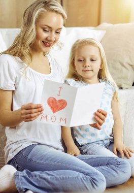 Güneşli dairede anneler günün kutlu olsun. Çocuk kızı annesini tebrik ediyor ve ona kalp çizimiyle kartpostal atıyor. Aile kavramı.
