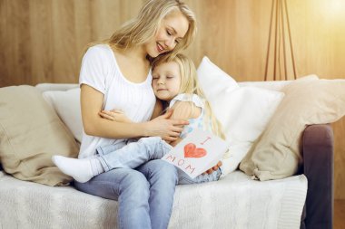 Güneşli dairede anneler günün kutlu olsun. Çocuk kızı annesini tebrik ediyor ve ona kalp çizimiyle kartpostal atıyor. Aile kavramı.