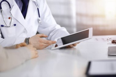 Bilinmeyen bir erkek doktor ve hasta kadın karanlık bir klinikte tablet bilgisayar kullanırken bir şeyi tartışıyor, arka planda ışık parlıyor. Hastanedeki en iyi sağlık hizmeti, ilaç, salgın durdurma.