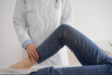 Doktor ve hasta klinikte olağan sağlık kontrolündeler. Terapist genç bir kadının dizini muayene ediyor. Tıp konsepti .