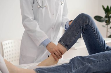 Doktor ve hasta klinikte olağan sağlık kontrolündeler. Terapist genç bir kadının dizini muayene ediyor. Tıp konsepti .