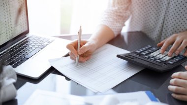 Müşteri için vergi sayarken hesap makinesi ve dizüstü bilgisayar kullanan kadın muhasebeci. İş denetimi kavramları.