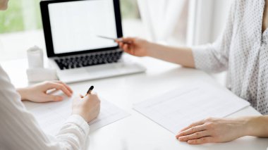 Beyaz masadaki vergileri saymak için dizüstü bilgisayar kullanan iki muhasebeci. İş kadını elinde kalemle ekranı işaret ediyor. İş denetimi ve finans alanında takım çalışması.