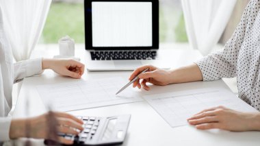 Ofisteki bir müşteriyle ya da meslektaşıyla vergi saymak için hesap makinesi ve dizüstü bilgisayar kullanan bir muhasebeci. İş denetimi ve finans alanında takım çalışması.