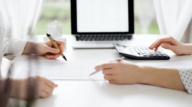 Ofisteki beyaz masada vergileri saymak için dizüstü bilgisayar ve hesap makinesi kullanan iki muhasebeci. İş denetimi ve finans alanında takım çalışması.