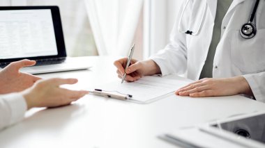Doktor ve hasta klinikteki beyaz masada oturup bir şeyler tartışıyorlar. Kadın hekim bir kayıt formunu doldururken dinliyor. Tıp konsepti.