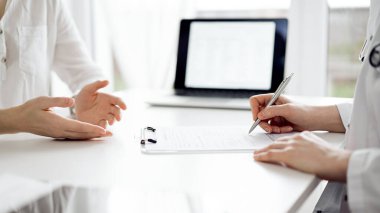 Doktor ve hasta klinikteki beyaz masada oturup bir şeyler tartışıyorlar. Kadın hekim bir kayıt formunu doldururken dinliyor. Tıp konsepti.