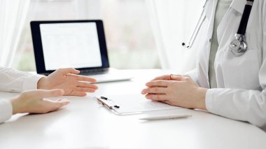 Doktor ve hasta klinikteki beyaz masada oturup bir şeyler tartışıyorlar. Kadın hekim bir kayıt formunu doldururken dinliyor. Tıp konsepti.