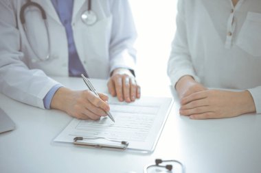 Doktor ve hasta klinikteki masada yan yana oturuyorlar. Kadın doktorların ellerinin tıbbi geçmiş kayıtlarını doldurması ya da kontrol listesi üzerinde yoğunlaşacağız. Kapat. Tıp konsepti.