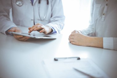 Doktor ve hasta klinikteki masada yan yana oturuyorlar. Kadın doktorların elleri tablet bilgisayarın dokunmatik dokunmatik pedini işaret ediyor, kapat. Tıp konsepti.